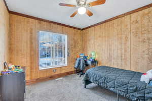 Bedroom with a ceiling fan, carpet, visible vents, baseboards, and wood walls