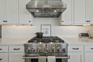 Kitchen featuring white cabinetry, tasteful backsplash, extractor fan, and stainless steel range