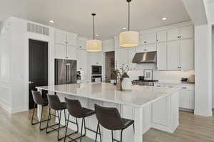 Kitchen with under cabinet range hood, appliances with stainless steel finishes, and white cabinets