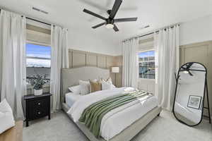 Bedroom featuring visible vents, light colored carpet, wainscoting, and a decorative wall