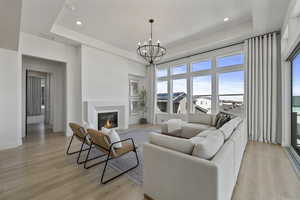 Living area with light wood-type flooring, a tray ceiling, a fireplace, baseboards, and a chandelier