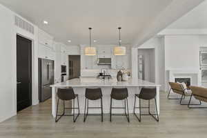 Kitchen featuring light wood-type flooring, decorative backsplash, appliances with stainless steel finishes, custom lighting