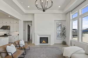 Living room with baseboards, light wood-style flooring, recessed lighting, a fireplace, and a raised ceiling