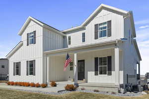 Modern farmhouse featuring a porch, board and batten siding, and fenceModern farmhouse with a front yard and board and batten siding and covered Porch