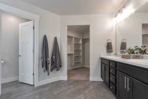 Full bathroom with a walk in closet, double vanity, baseboards, and a sink