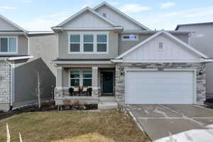 View of front facade featuring board and batten siding, covered porch, driveway, stone siding, and an attached garage