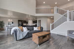 Living room with stairway, wood finished floors, visible vents, an inviting chandelier, and a towering ceiling