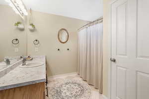 Full bath featuring a shower with shower curtain, baseboards, vanity, and tile patterned floors