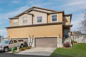 View of front facade featuring a garage, stone siding, concrete driveway, and stucco siding