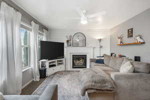 Living area featuring wooden walls, baseboards, carpet floors, a glass covered fireplace, and a ceiling fan
