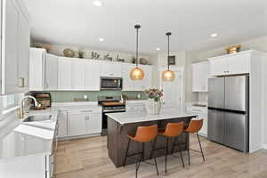 Kitchen featuring a sink, stainless steel appliances, white cabinets, light wood-type flooring, and a center island