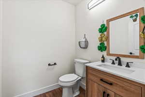 Half bath with vanity, toilet, wood finished floors, and baseboards