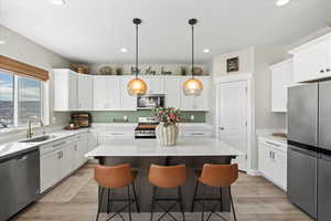 Kitchen with a center island, appliances with stainless steel finishes, a kitchen breakfast bar, white cabinetry, and a sink
