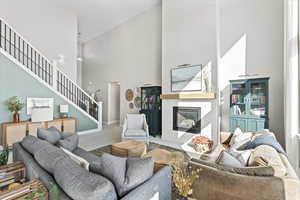 Carpeted living area featuring stairway, baseboards, a brick fireplace, and a towering ceiling