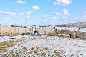 Yard covered in snow featuring a playground and fence