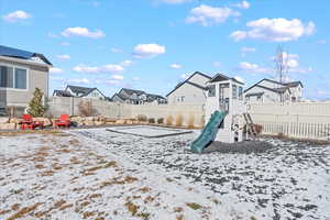 Snowy yard featuring a residential view, a playground, and a fenced backyard