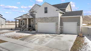 View of front of house featuring stone siding, board and batten siding, concrete driveway, and fence