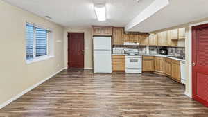 Kitchen featuring dark wood-type flooring, white appliances, light countertops, decorative backsplash, and baseboards