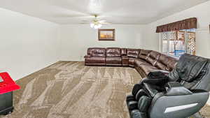 Carpeted living area with baseboards, a textured ceiling, and ceiling fan