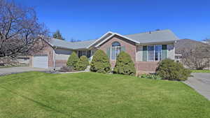 Ranch-style house featuring concrete driveway, brick siding, a front lawn, a shingled roof, and a garage