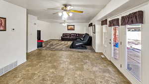 Living room with visible vents, baseboards, a textured ceiling, and ceiling fan