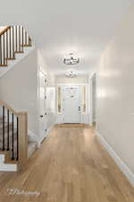 Foyer with baseboards, an inviting chandelier, stairs, and light wood finished floors