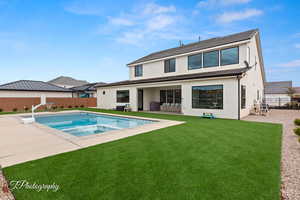 Rear view of property with a pool with connected hot tub, stucco siding, a lawn, a fenced backyard, and a patio