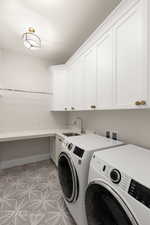 Washroom with washing machine and clothes dryer, cabinet space, baseboards, and a sink