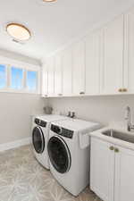 Washroom featuring visible vents, baseboards, washer and dryer, cabinet space, and a sink