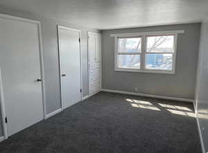 Unfurnished bedroom featuring multiple closets, a textured ceiling, baseboards, and dark colored carpet