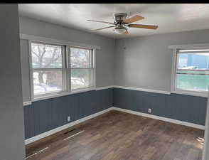 Spare room featuring a ceiling fan, visible vents, dark wood-style flooring, wainscoting, and a textured ceiling