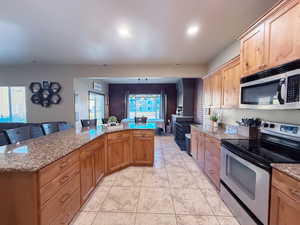 Kitchen with light tile patterned floors, light stone countertops, open floor plan, and stainless steel appliances