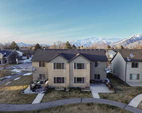 View of front of property featuring a patio, a front yard, roof with shingles, stucco siding, and a mountain view