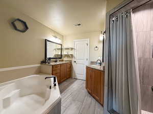 Full ensuite bathroom featuring visible vents, two vanities, a jetted tub, and a sink
