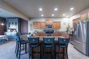 Kitchen with a kitchen island, recessed lighting, appliances with stainless steel finishes, brown cabinetry, and light tile patterned floors