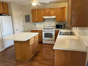 Kitchen featuring a sink, electric panel, under cabinet range hood, white appliances, and light countertops