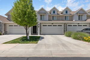 Townhome / multi-family property featuring driveway, stone siding, and roof with shingles