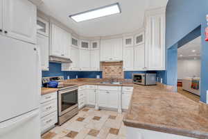 Kitchen with white cabinetry, under cabinet range hood, appliances with stainless steel finishes, and a sink