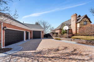 View of home's exterior featuring brick siding, fence, a chimney, decorative driveway, and a garage