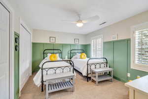 Bedroom featuring a decorative wall, light colored carpet, visible vents, and a wainscoted wall
