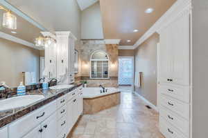 Full bath with stone tile flooring, ornamental molding, a garden tub, and a sink