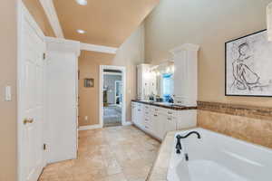 Full bathroom with ornamental molding, stone tile flooring, baseboards, a bath, and vanity