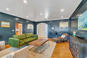 Living area with a wainscoted wall, ornamental molding, light wood-style flooring, recessed lighting, and arched walkways