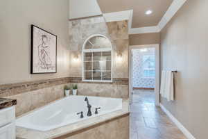 Bathroom with crown molding, stone tile floors, a garden tub, and baseboards