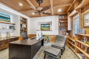 Office space featuring built in shelves, beam ceiling, coffered ceiling, wainscoting, and ceiling fan