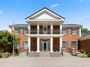 Neoclassical / greek revival house featuring a balcony, covered porch, brick siding, and french doors
