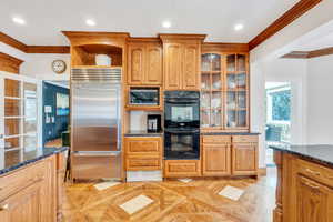 Kitchen featuring dark stone countertops, glass insert cabinets, built in appliances, and ornamental molding
