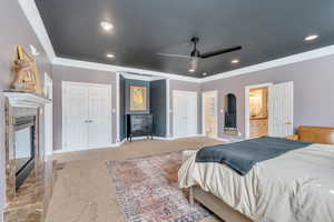 Bedroom featuring carpet, baseboards, ornamental molding, a tile fireplace, and two closets