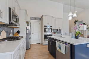 Kitchen featuring a kitchen island with sink, a sink, stainless steel appliances, white cabinets, and light wood finished floors