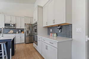 Kitchen with backsplash, stainless steel appliances, light wood-style floors, and light countertops